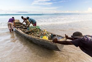 men pushing a small wooden boat filled with fishing nets.